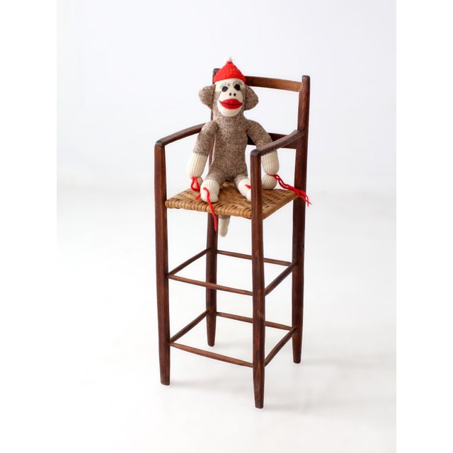Charming antique child’s high chair crafted with a tall wooden frame, slender stretchers, open arms, and a woven seat. The...