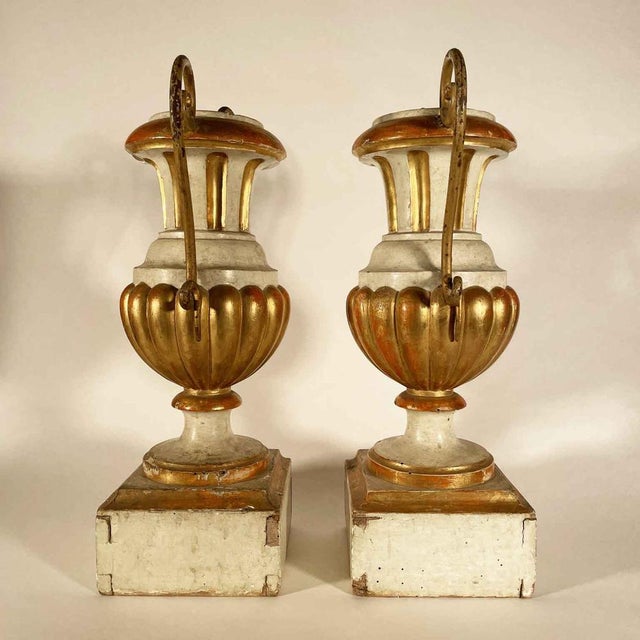 A pair of lacquered and gilded wooden palm holders with wrought and gilded iron handles, resting on a prominent square...