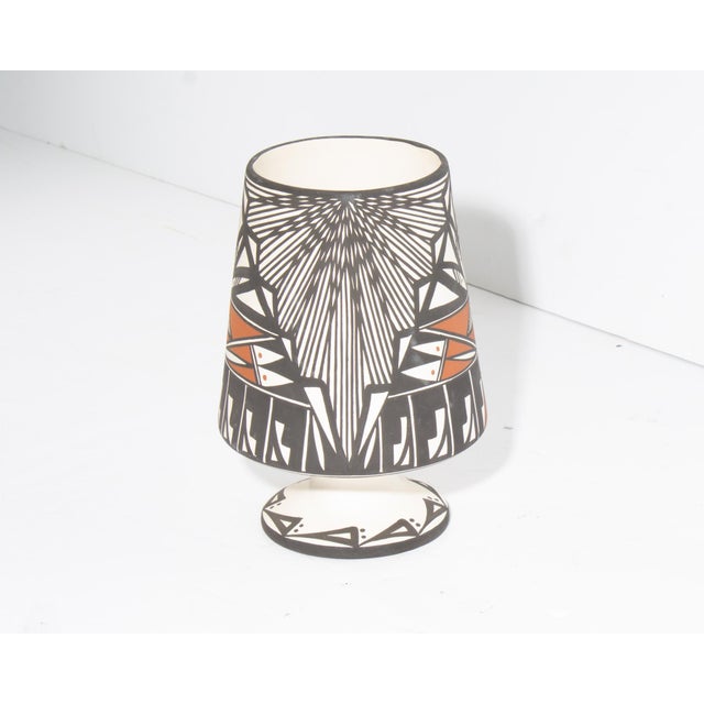 A footed vase by the Acoma Pueblo pottery D. Trujillo. The vase features an black and orange design against a white...