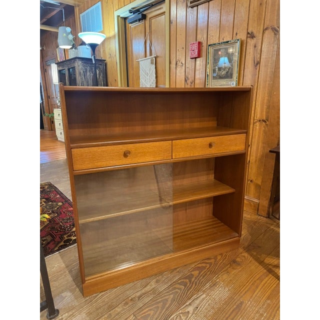 Mid-Century Modern Style Bookcase featuring an upper shelf, two drawers with round wooden knobs, and lower sliding glass...