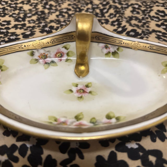This elegant, boat-shaped porcelain dish features a delicate hand-painted floral motif of pink roses and soft green...