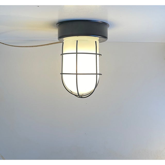 A cage flush mount ceiling or wall light in opaline glass and black painted metal. Great industrial or even submarine vibe...