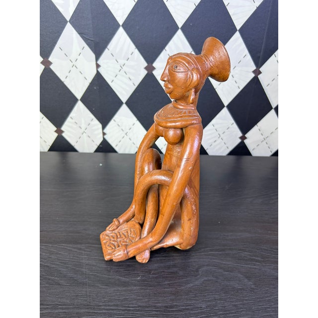 Vintage Indian terracotta sculpture depicting a stylized seated female figure with dramatically elongated arms and legs....