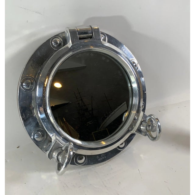 Authentic polished aluminum ship's porthole fitted with a glass mirror. Door is hinged and fitted with two dogbolts. The...