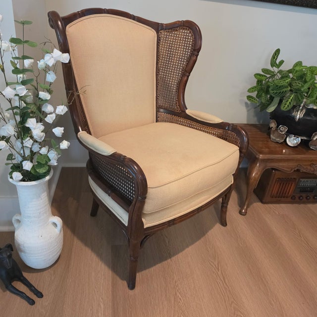 Bring a touch of refined Hollywood Regency flair to your space with this vintage wingback bergere chair manufactured by...