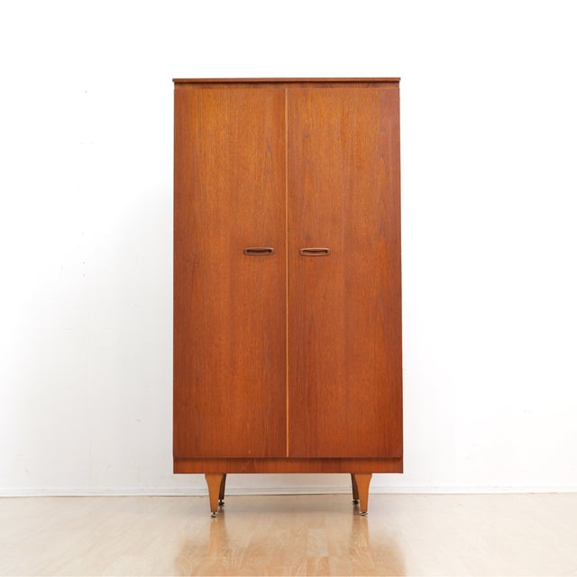 This vintage mid-century armoire was produced by Stonehill of London during the 1960s. Made from teak the two front hinged...