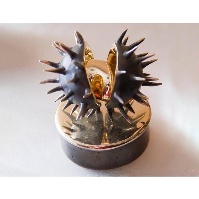 A contemporary still-life bronze of a chestnut splitting open in its spiny husk, the bristling case parting to reveal the...