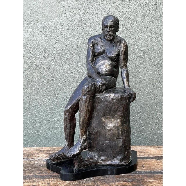 This vintage bronzed terracotta sculpture captures a contemplative seated male figure, perched thoughtfully atop a rough-...