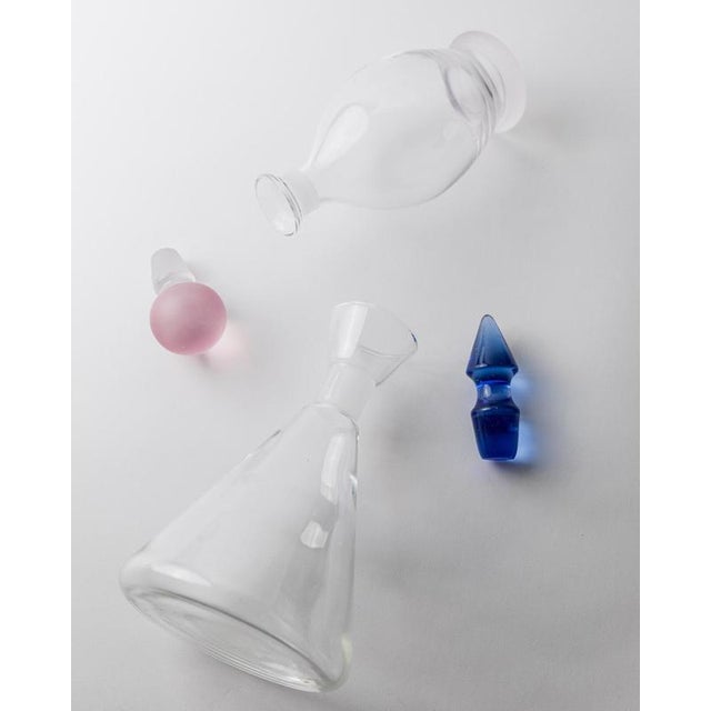 This vintage glass decanter set from the 1980s includes two sculptural pieces with striking color accents. One decanter is...