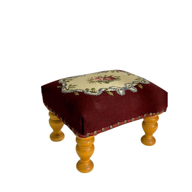 Charming vintage upholstered footstool featuring a rich burgundy color intricate floral needlepoint and beautifully turned...