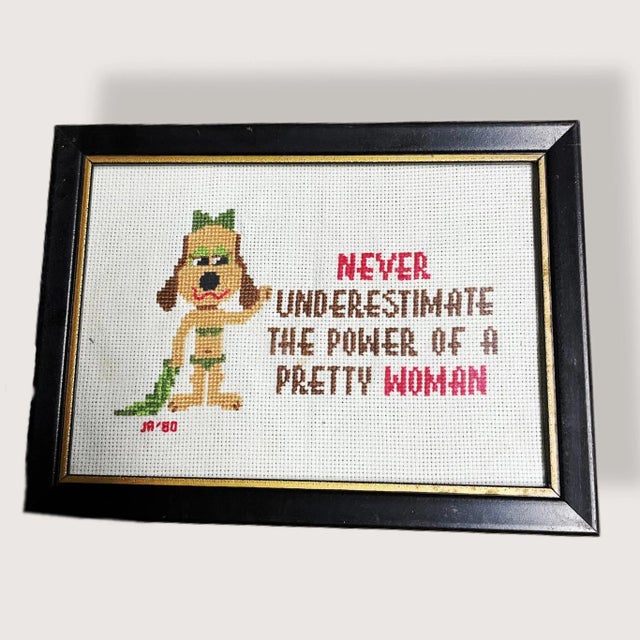 Vintage needlepoint that says “Never Underestimate the Power of a Pretty Woman” of a dog in a green bikini with lipstick....