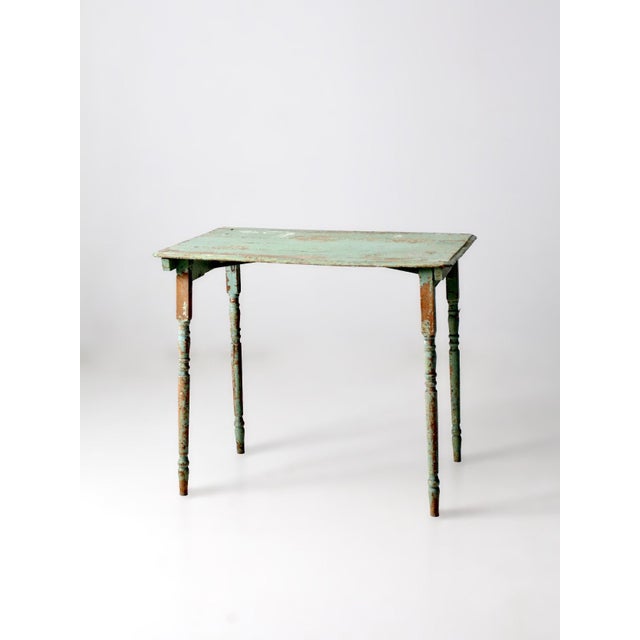 An early 20th century antique side table with beautifully timeworn green paint and classic turned legs. The plank top...
