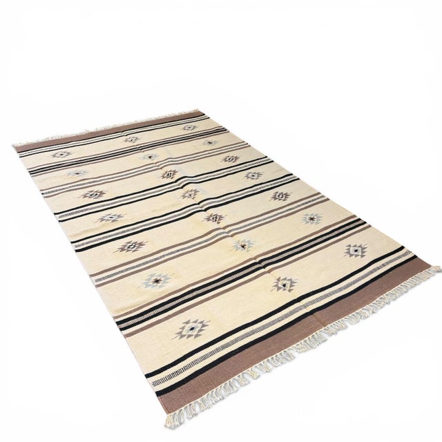A beautifully composed handwoven kilim rug from India, featuring a serene ivory field structured by narrow linear stripes...