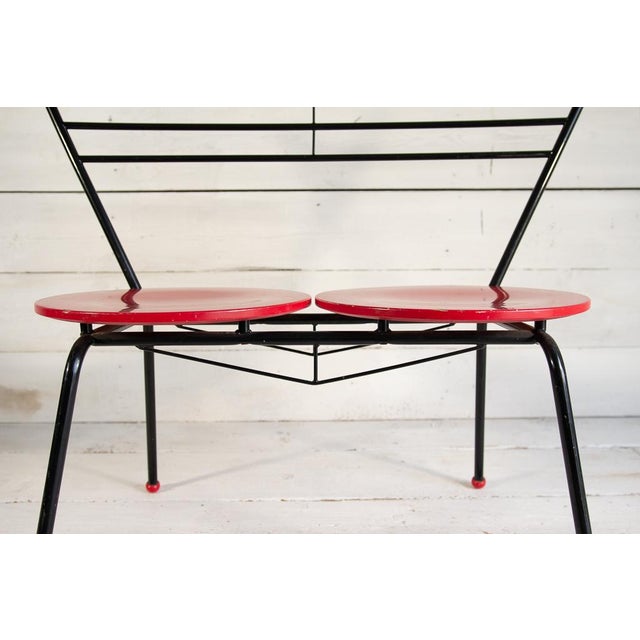 Two-seat round bench made of wood and metal. The frame, made of black painted metal with the slender features typical of...
