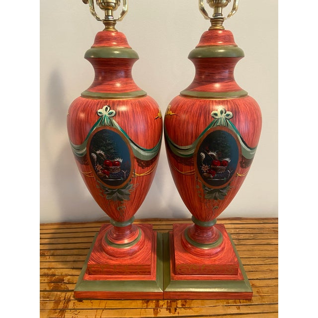 Pair of vintage urn-shaped red hand-painted lamps featuring a beautiful blend of greens, blues, and gold accents. Each...