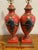 Pair of vintage urn-shaped red hand-painted lamps featuring a beautiful blend of greens, blues, and gold accents. Each...