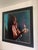 This oil painting on aluminum depicts a figure holding a candle, its warm light illuminating her face against a backdrop...