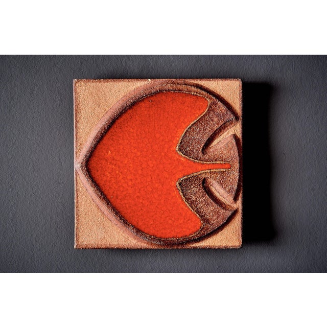Decorative ceramic wall tile by Søholm, with a raised fish motif in warm orange and brown glazes. The piece has a textured...