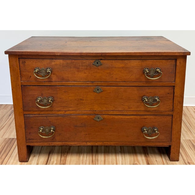 Handsome antique three drawer wood commode. Features rich natural finish with stunning original brass hardware. Three...