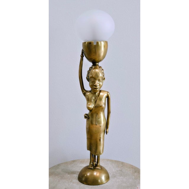 A striking vintage African brass figural table lamp featuring a graceful standing female figure balancing a bowl-form...