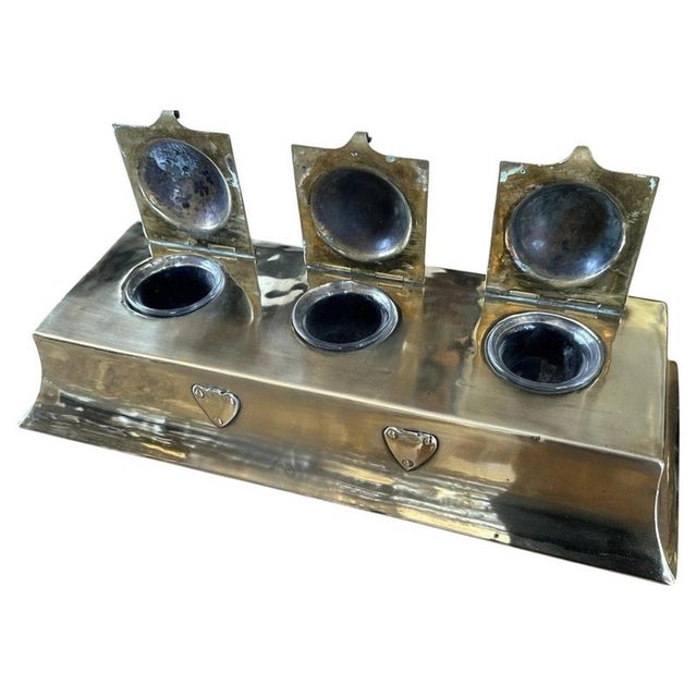 Three domed, hinged lids set flush into a flared rectangular brass casing distinguish this substantial Arts & Crafts desk...