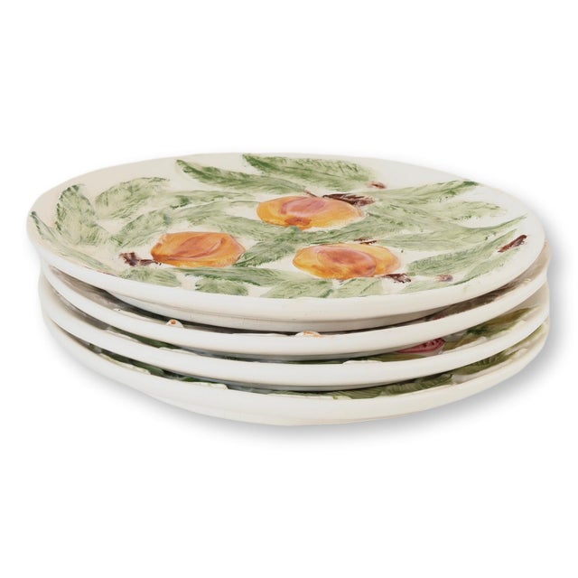 Set of four midcentury faience plates, each featuring a hand-painted fruit motif including peach, grape, strawberry, and...