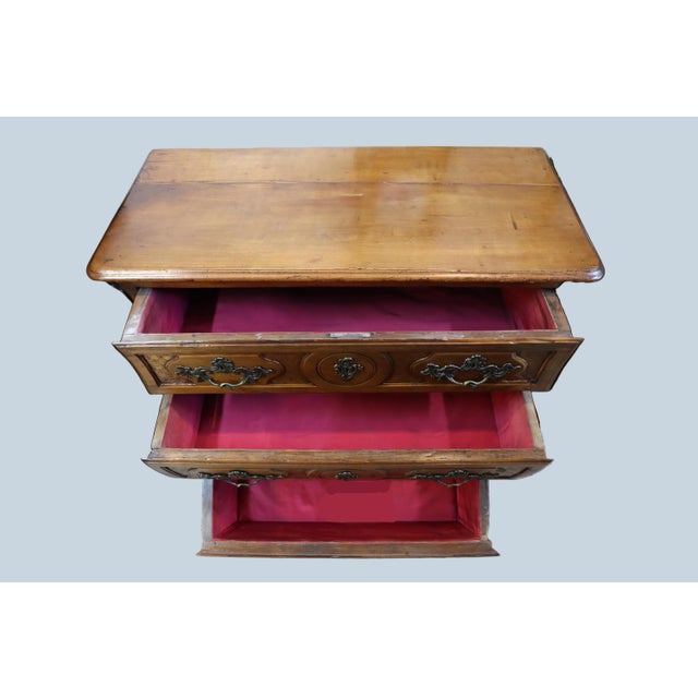 Charming and stunning three-drawer bombe commode constructed out of walnut wood. This dresser is adorned with intricately...