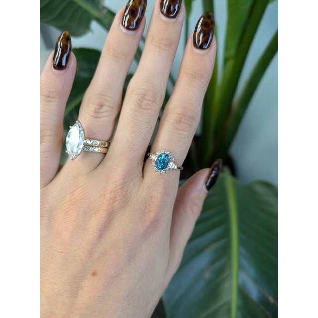 A 3.47-carat cambodian blue zircon oval sits at the centre of this solid 14K rose gold ring, framed by sixteen earth-mined...