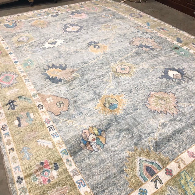 A refined modern Turkish Oushak rug featuring a soft gray-blue field framed by a warm beige border, with large-scale...