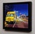 This artwork depicts a vibrant yellow hot dog truck parked on a bustling city street, illuminated by the glow of...