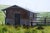 This oil painting depicts a rustic structure nestled amidst lush green grass, evoking a sense of tranquility and...
