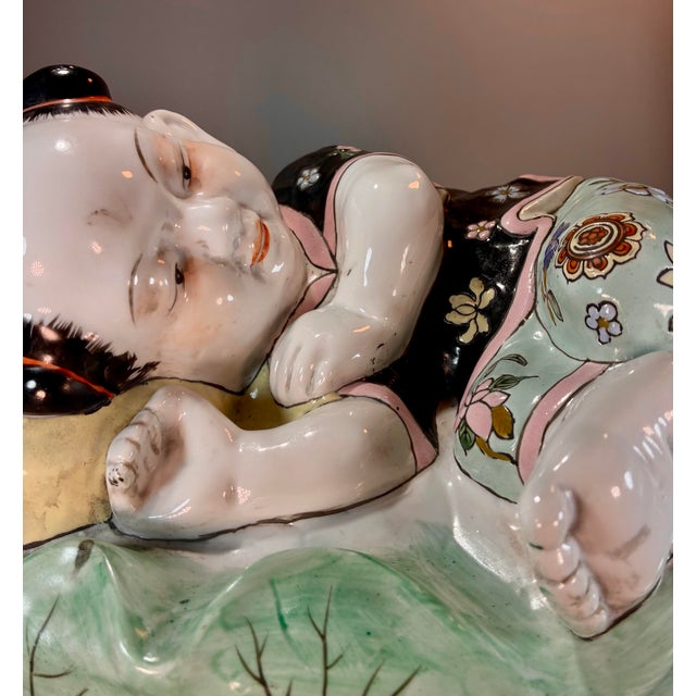 Chinese porcelain sculpture or pillow depicting a child sleeping with intricate floral and patterned clothing details.