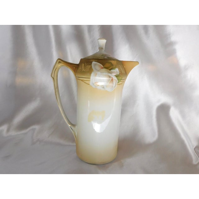 This is a cream and gold Reinhold Schlegelmil chocolate pot. It has gold trim, a white floral design and a matching lid....