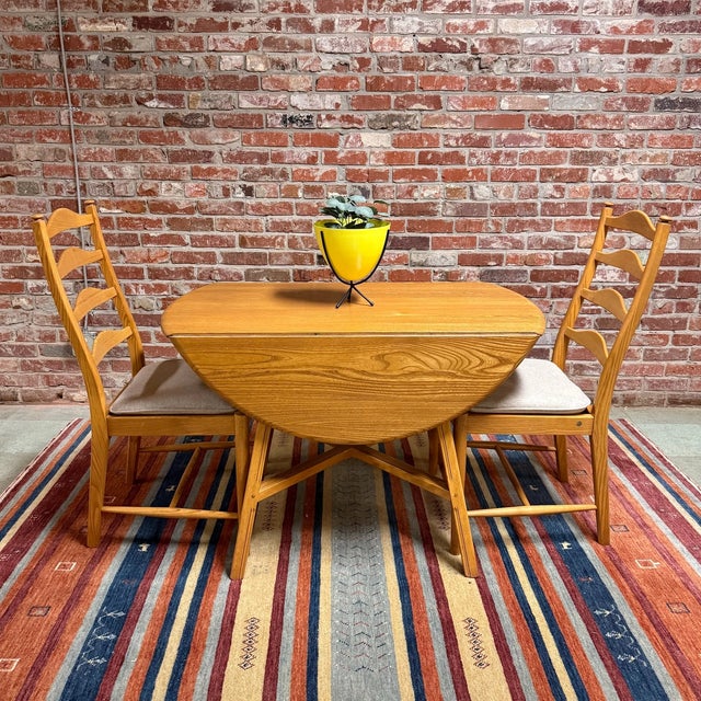 Vintage Ercol dining set featuring a Model 377 drop-leaf table with four Model 823 Penn ladder back dining chairs. Made in...