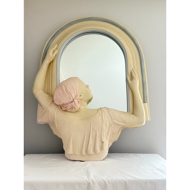 Monumental sculptural wall mirror featuring a neoclassical female figure integrated into an arched architectural form....