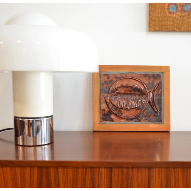 Wall-mounted ceramic sculpture depicting a stylized fish, mounted on a wooden plaque. The glazed surface shows rich shades...