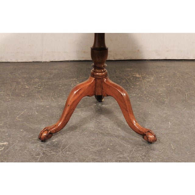 An English mahogany wood tilt top pedestal table from the 19th century. This antique guéridon table from England features...
