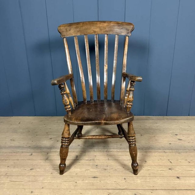 Antique brown English Windsor armchair made of elm, circa 1900. The high back features graceful curved spindles, and the...
