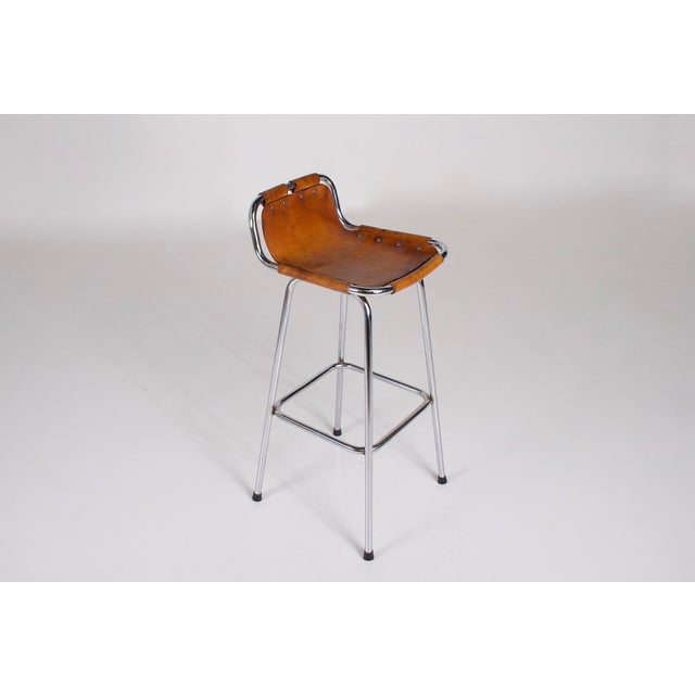A short-back bar stool, often attributed to charlotte perriand. Cognac leather seat riveted to a chromed tubular frame,...