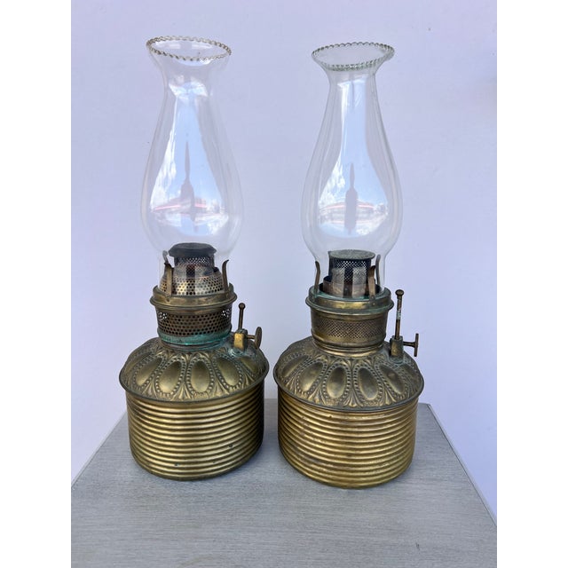 Antique Victorian-era brass oil/kerosene fonts featuring ribbed cylindrical lower reservoirs and embossed decorative...