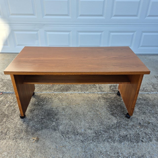 This is a circa 1970s Danish modern teak veneer rolling desk. The rolling table has a rectangular top with straight sides...