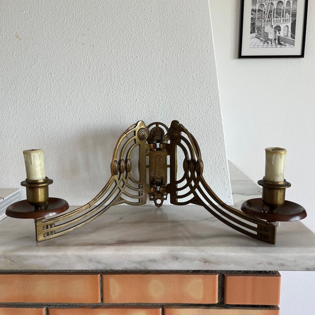A striking vintage double wall sconce in aged brass, designed around a dramatic symmetrical composition. Two candle-style...