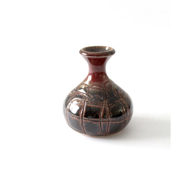 This vintage handmade studio pottery vase features a bulbous base and a narrow bottleneck, creating an elegant silhouette....
