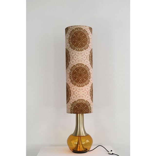 This floor lamp was made in the 1970s. It consists of an illuminated glass foot and a fabric screen with a floral pattern....