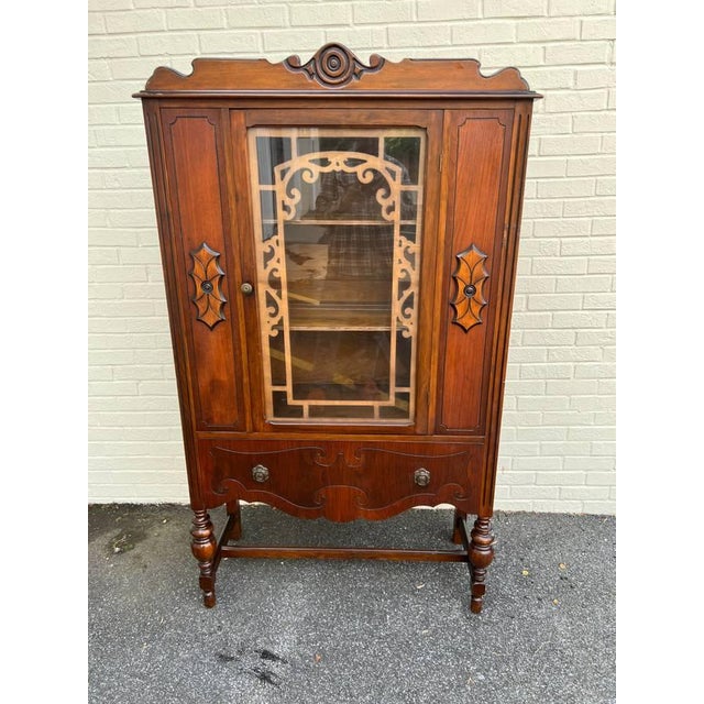 Early 20th Century Jacobean Revival Style Walnut Display China Cabinet It features hand carved t with one drawer and wood...