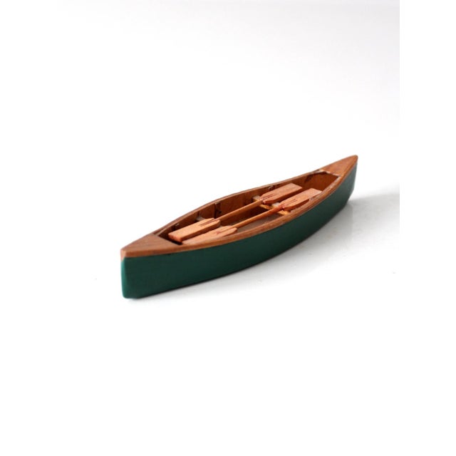 Vintage handmade wooden canoe model featuring a painted green hull, natural wood interior, and four miniature paddles. Its...