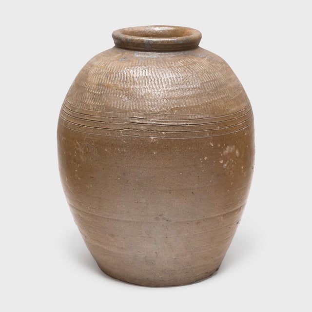 Coated inside and out with an olive green glaze, this large ceramic jar from early 20th century Thailand was originally...