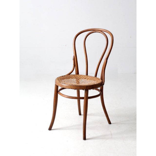 This antique bentwood café chair features an arched bentwood back, softly curved legs, and a warm wood tone that brings...