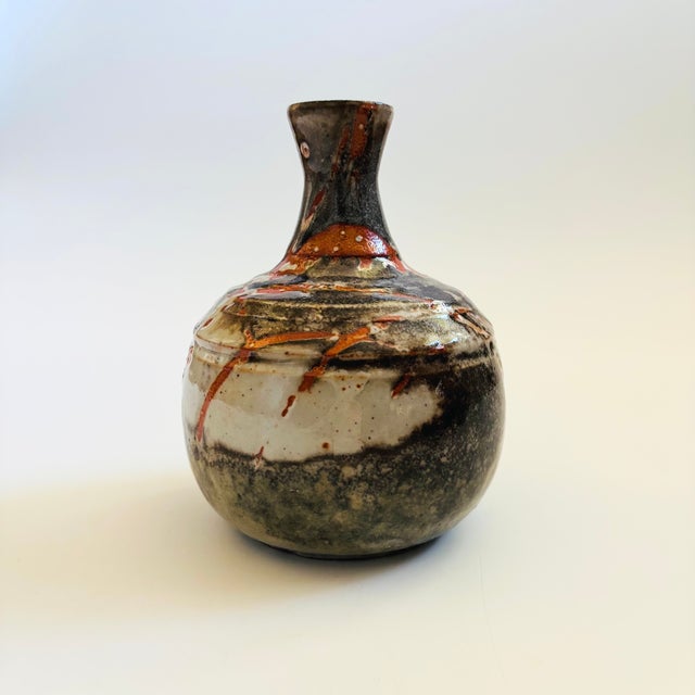 A beautiful vintage studio pottery vase. Features overlapping glazes in gray with orange accents. Measures 4.5"Dia x 6.5"H