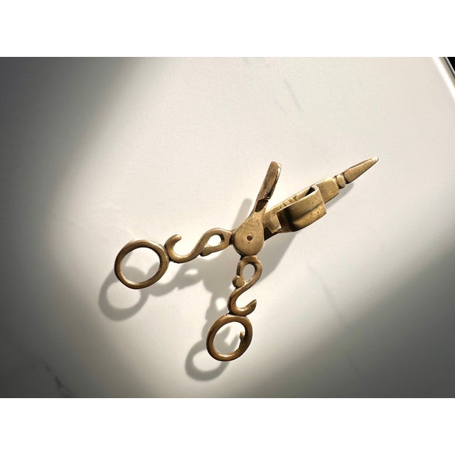 A wonderfully sculptural vintage brass candle wick trimmer and snuffer featuring ornate scrolling handles, oversized...